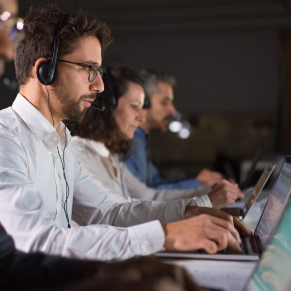 Side view of confident call center operator talking with client. Caucasian young man in eyeglasses typing on laptop while serving client. Call center concept